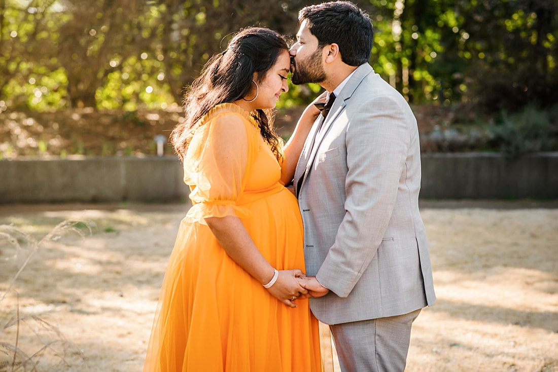 husband kissing pregnant wife's forehead at memphis botanic garden