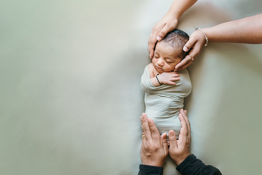 newborn baby boy with mom and dad's hands holding him during newborn photos in memphis